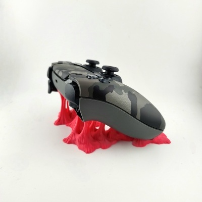 Comando de videojogo camuflado cinza e preto em base vermelha decorativa