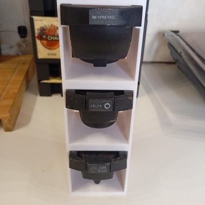 Organizador branco com cápsulas de café preto marcadas com NESPRESSO, DELTA e CAFE MOIDO