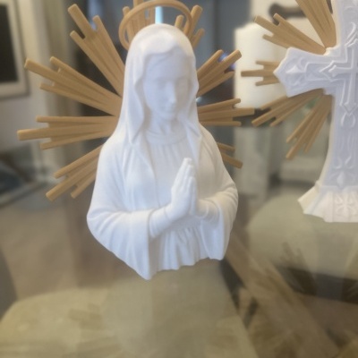 Estátua branca da Virgem Maria com halo dourado e raios, em interior