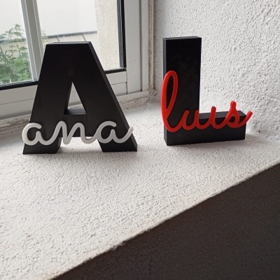 Letras decorativas pretas com nomes ana e luis em branco e vermelho numa superfície branca junto a uma janela
