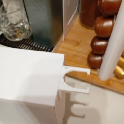 Máquina de café branca com suporte de cápsulas e cápsulas marrons ao lado