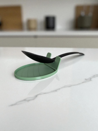 Descanso de colher verde em silicone com colher preta num balcão de cozinha.