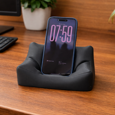 Suporte preto para smartphone em forma de mini sofá sobre mesa de madeira
