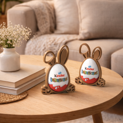 Ovos de chocolate Kinder com orelhas e patas de coelho numa mesa de madeira junto a livros e vaso com flores.