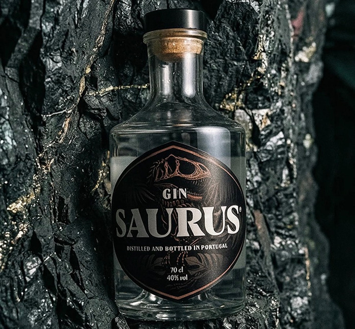 Gin Saurus: Um Gin Premium com ADN da Lourinhã Garrafas de gin Saurus transparentes com rótulo preto em fundo rochoso escuro.