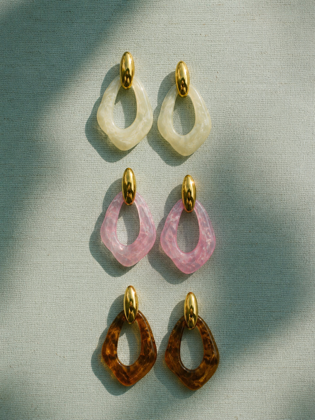 BRINCOS XARÉU Três pares de brincos com pendentes geométricos em creme, rosa e castanho com base oval dourada