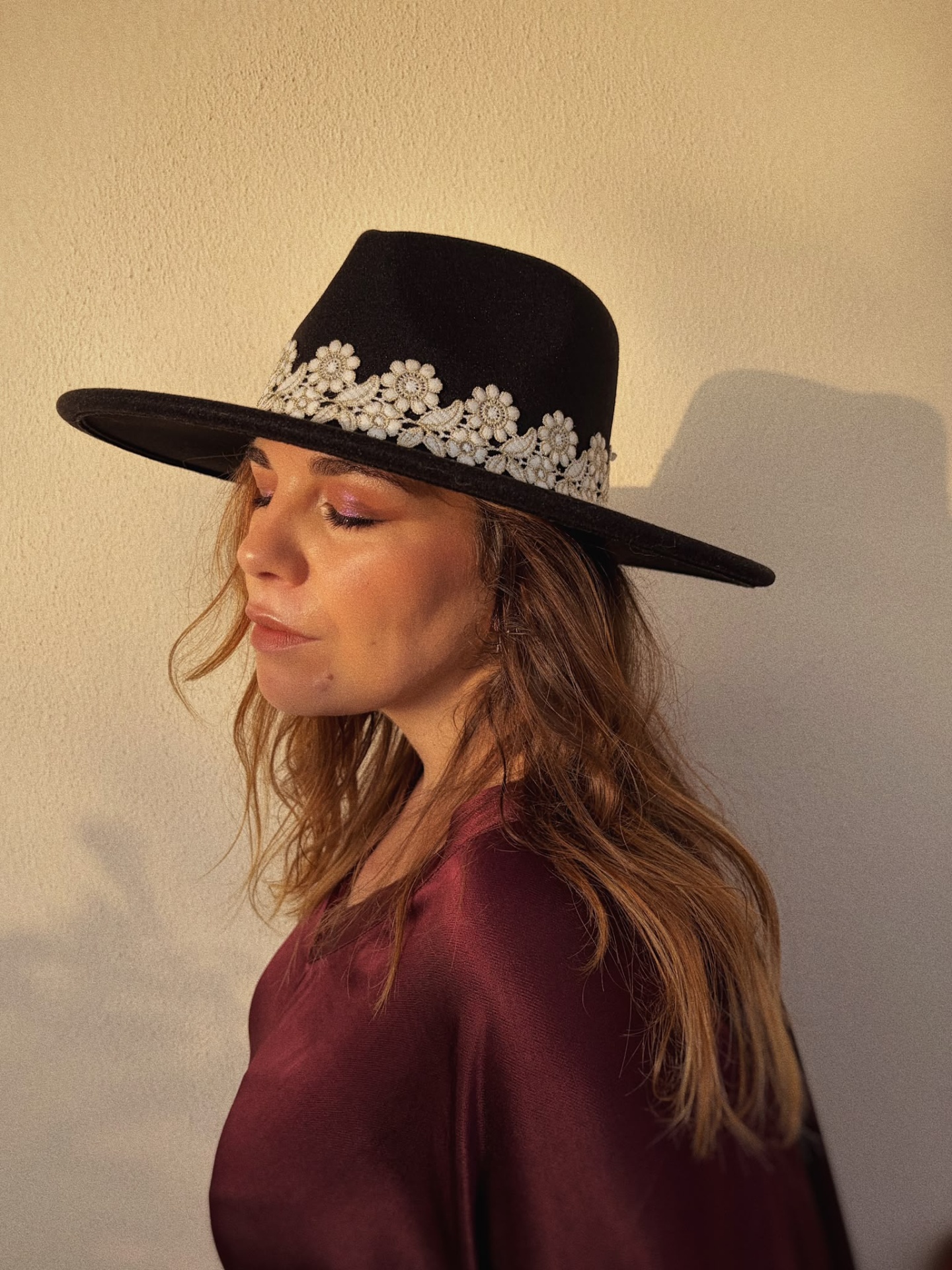 CHAPÉU AMAL PRETO Mulher de perfil com chapéu preto de aba larga e flores brancas bordadas