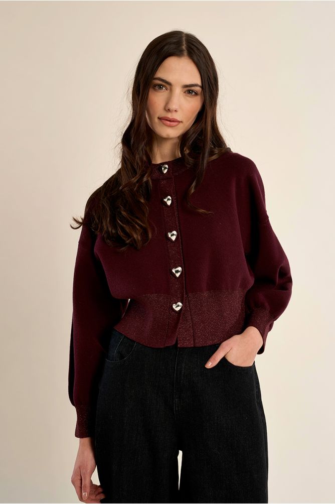 CASACO AMÉRICA BORDEAUX Cardigan bordeaux com botões de coração e calças pretas numa modelo.