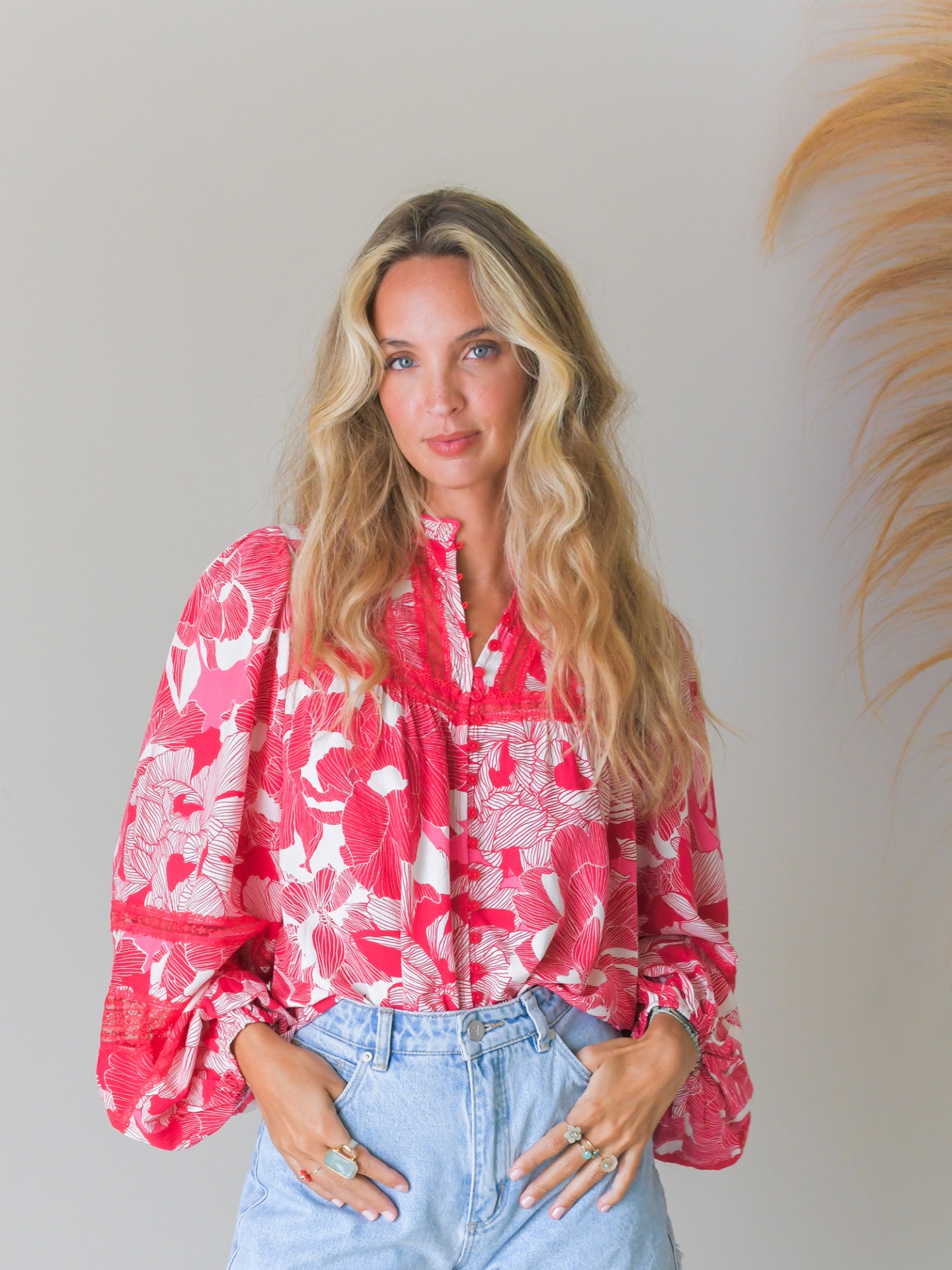 BLUSA SOULINA Mulher com blusa floral vermelha e branca e calças de ganga azuis.