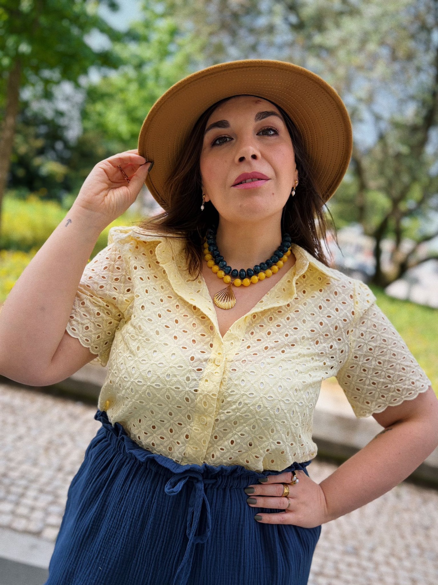 CAMISA WAVERINE AMARELO Mulher com blusa amarela, calças ou saia azul, chapéu castanho, colar e joias