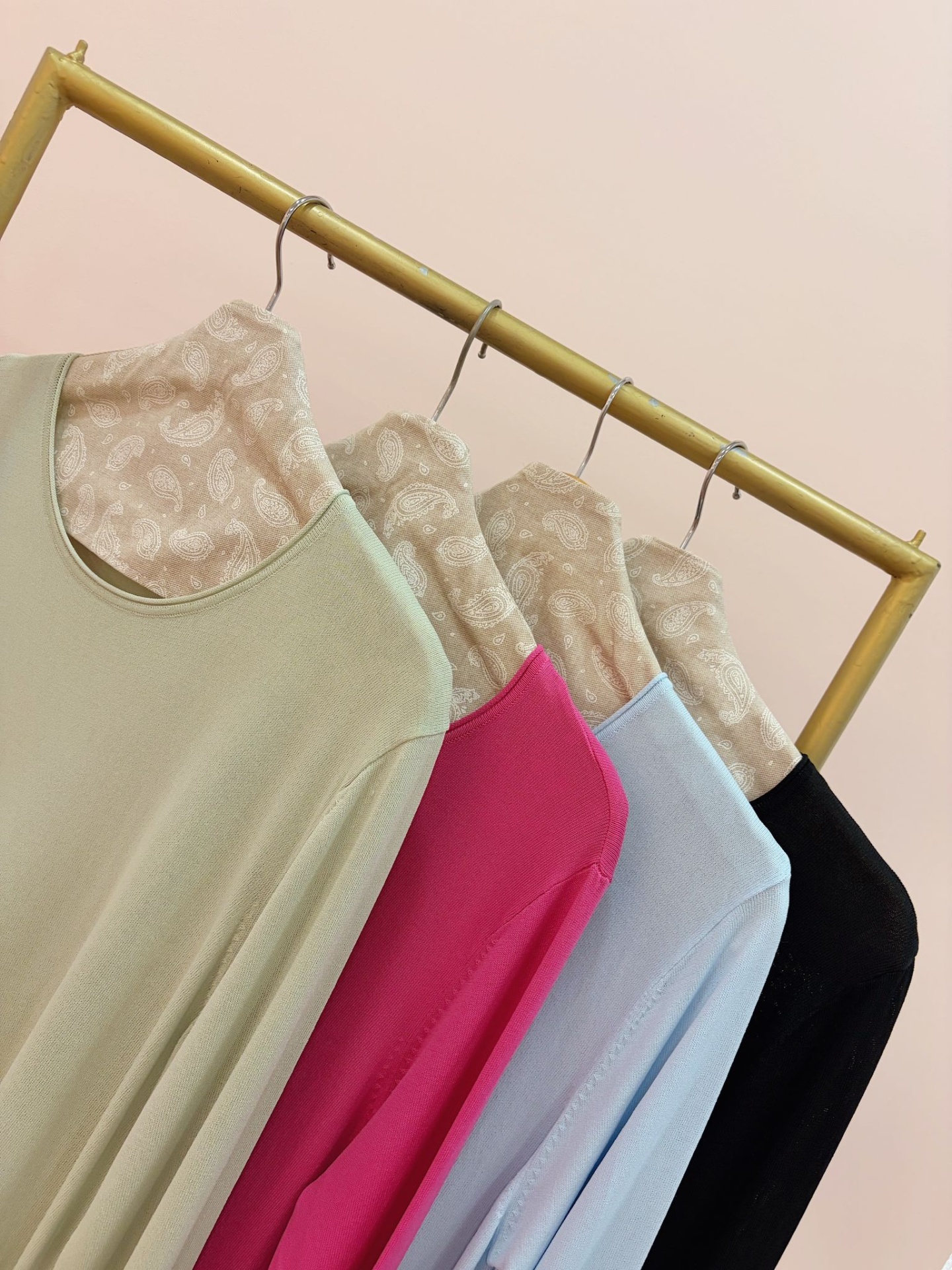 CAMISOLA SESIRA Quatro camisolas de manga comprida em cinco cores penduradas numa estrutura metálica dourada