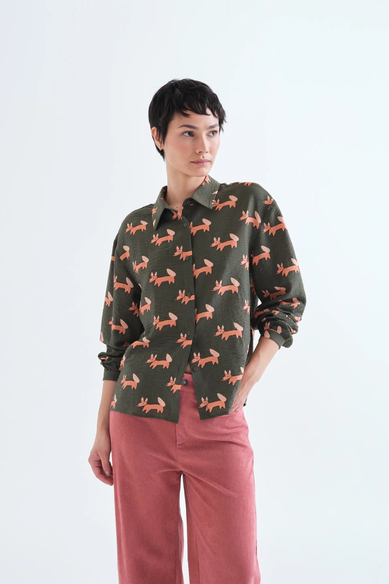 CAMISA VOLPE Mulher com camisa verde estampada de raposas cor de rosa e calças cor-de-rosa de veludo cotelê.