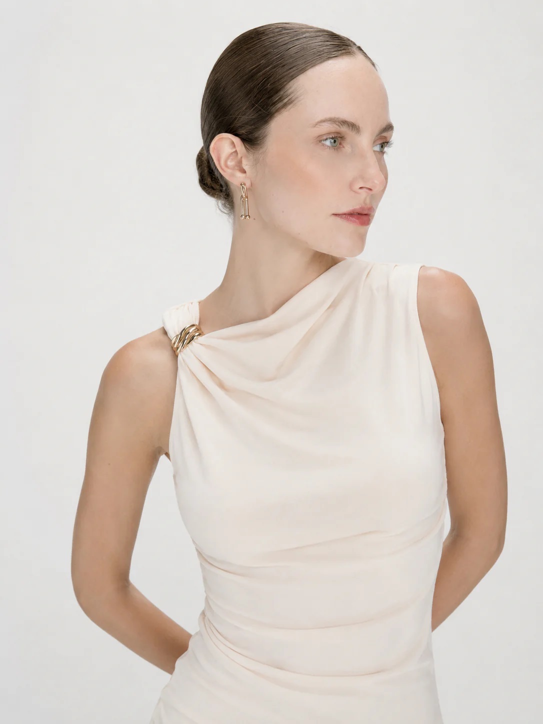 TOP WAGNER PÉROLA Mulher com vestido creme de um ombro só e brincos dourados
