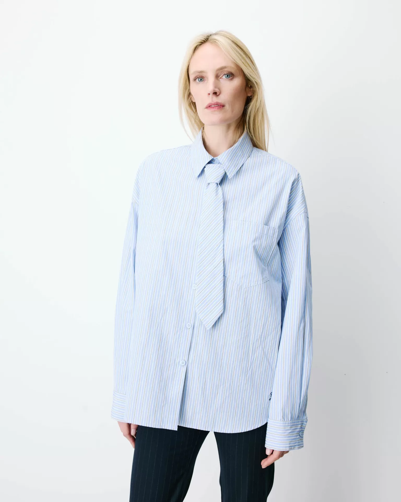 CAMISA ATHENA AZUL Camisa azul claro às riscas com bolso e gola clássica, vista da cintura para cima