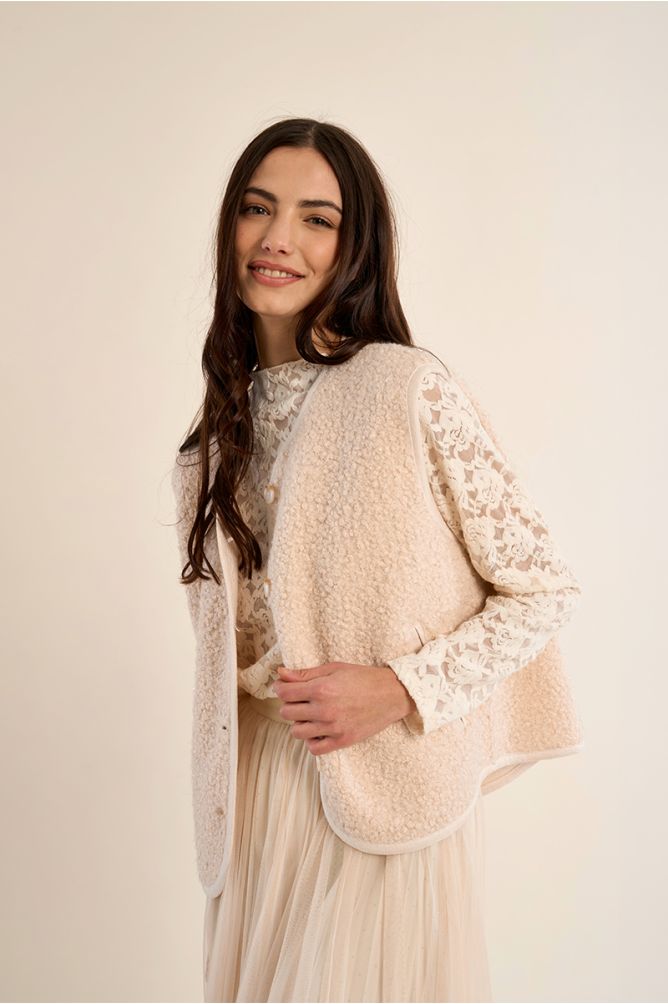 BLUSA BERTILDE PÉROLA Mulher com colete bege peludo, blusa rendada branca e saia branca fluida