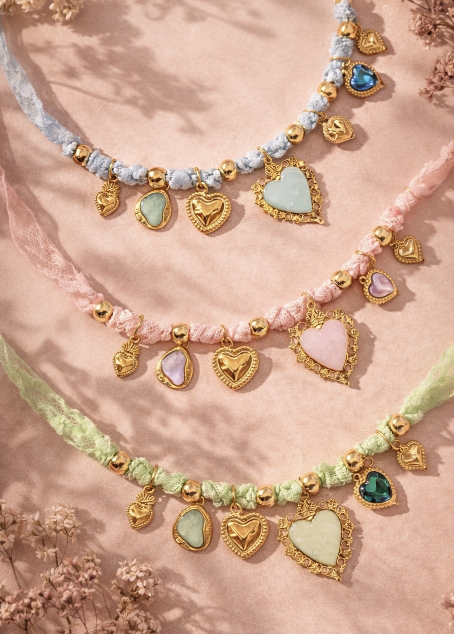 COLAR SEPHORA Colares com fita rendada e pendentes em formato de coração em várias cores sobre fundo rosa.