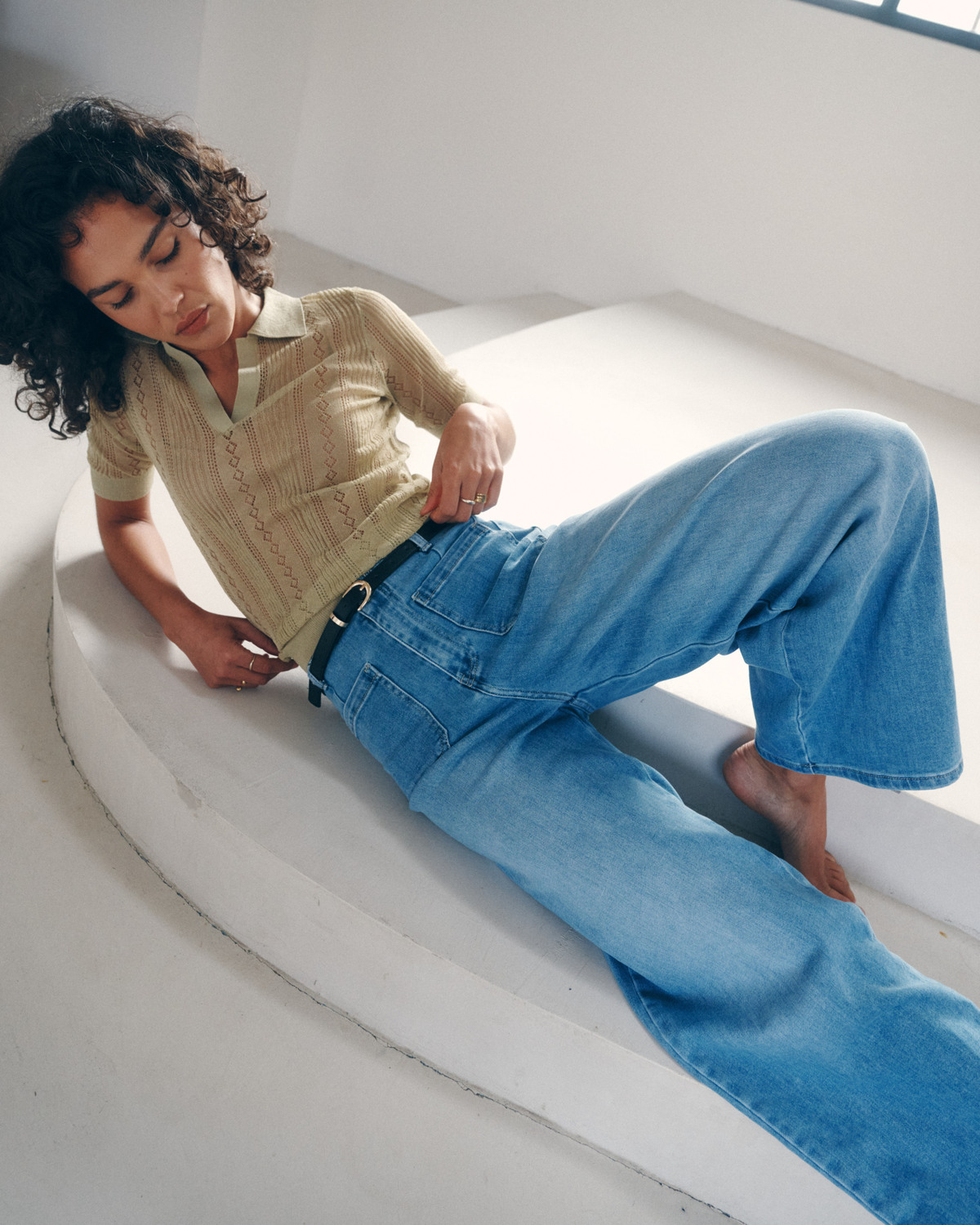 JEANS SIMONETA Mulher deitada com camisola bege de malha e calças de ganga largas azuis.