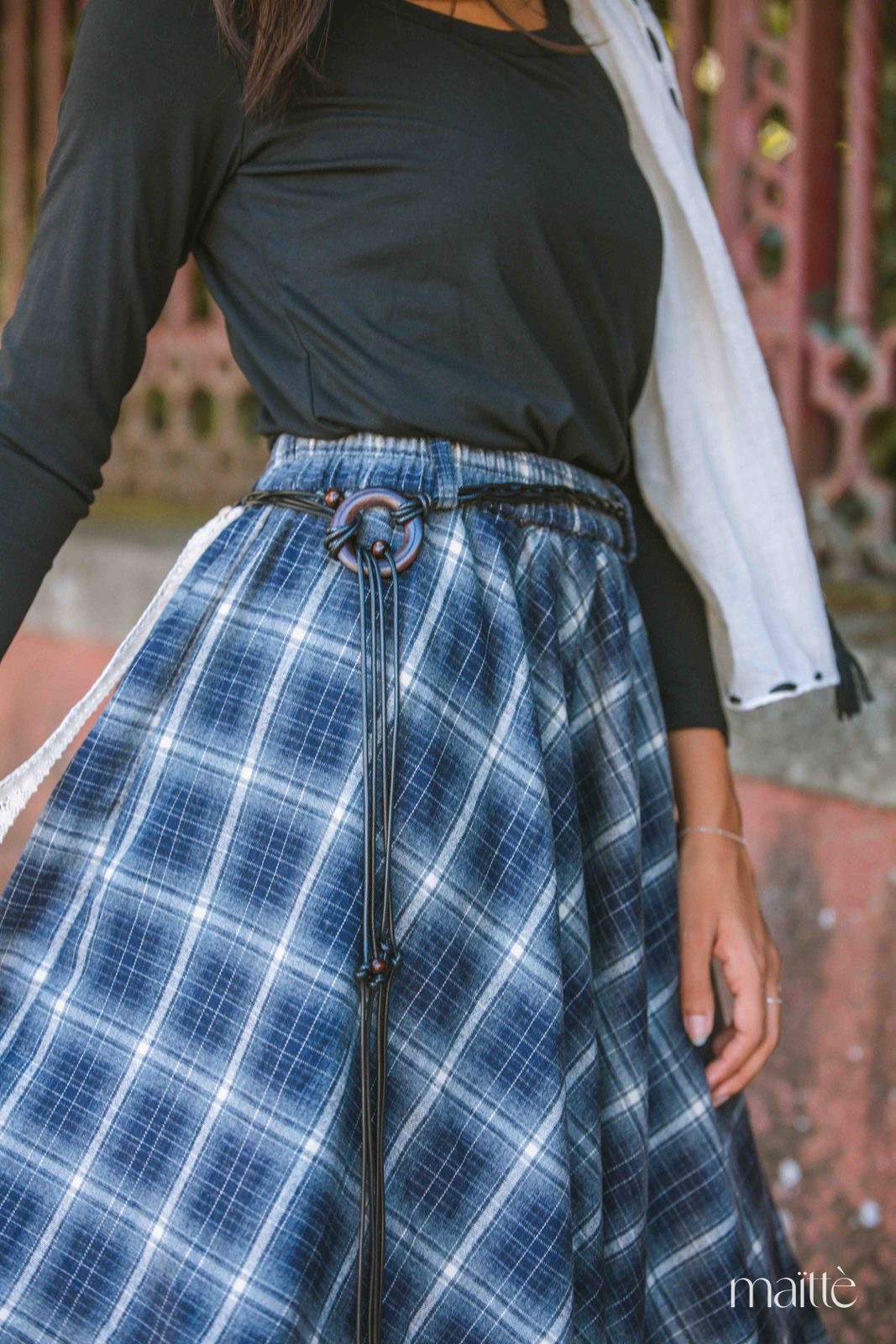 SAIA CAMÉLIA Saia xadrez azul e branco com cinto preto e blusa preta em ambiente urbano