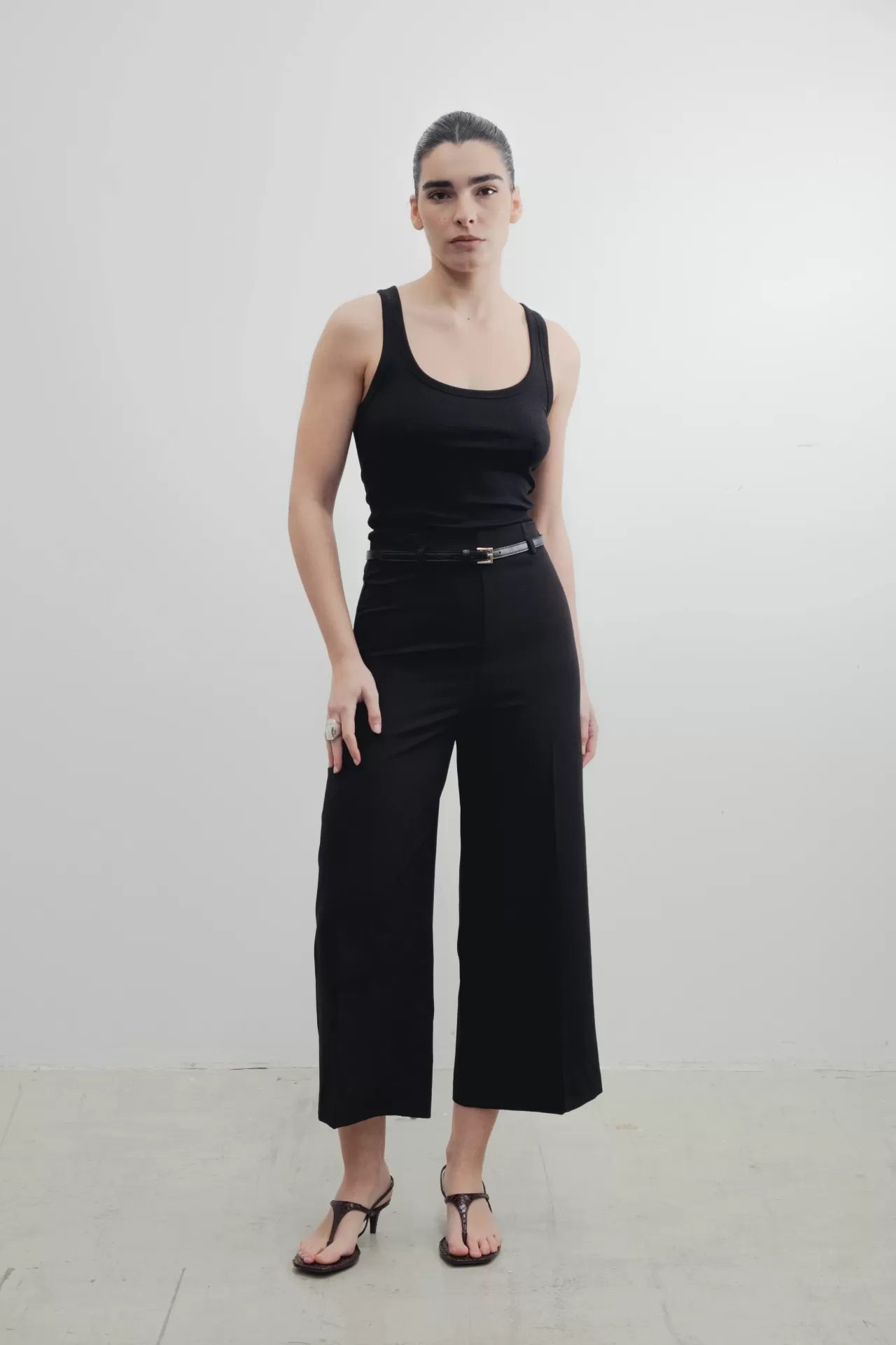 CALÇAS SABINA Mulher em top preto e calças pretas de perna larga com sandálias pretas