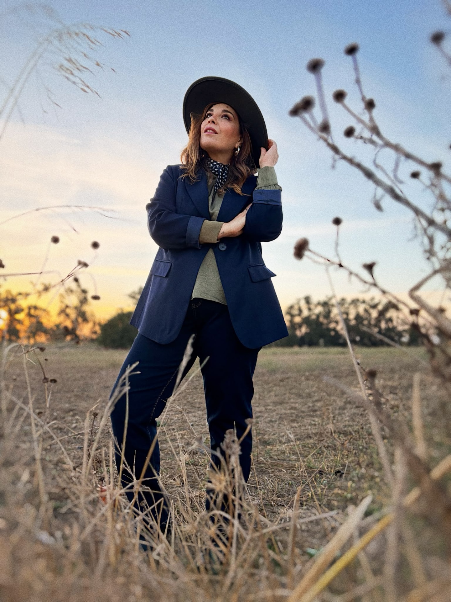 BLAZER BEULAH Mulher com casaco azul, calças azuis e chapéu preto em campo ao entardecer