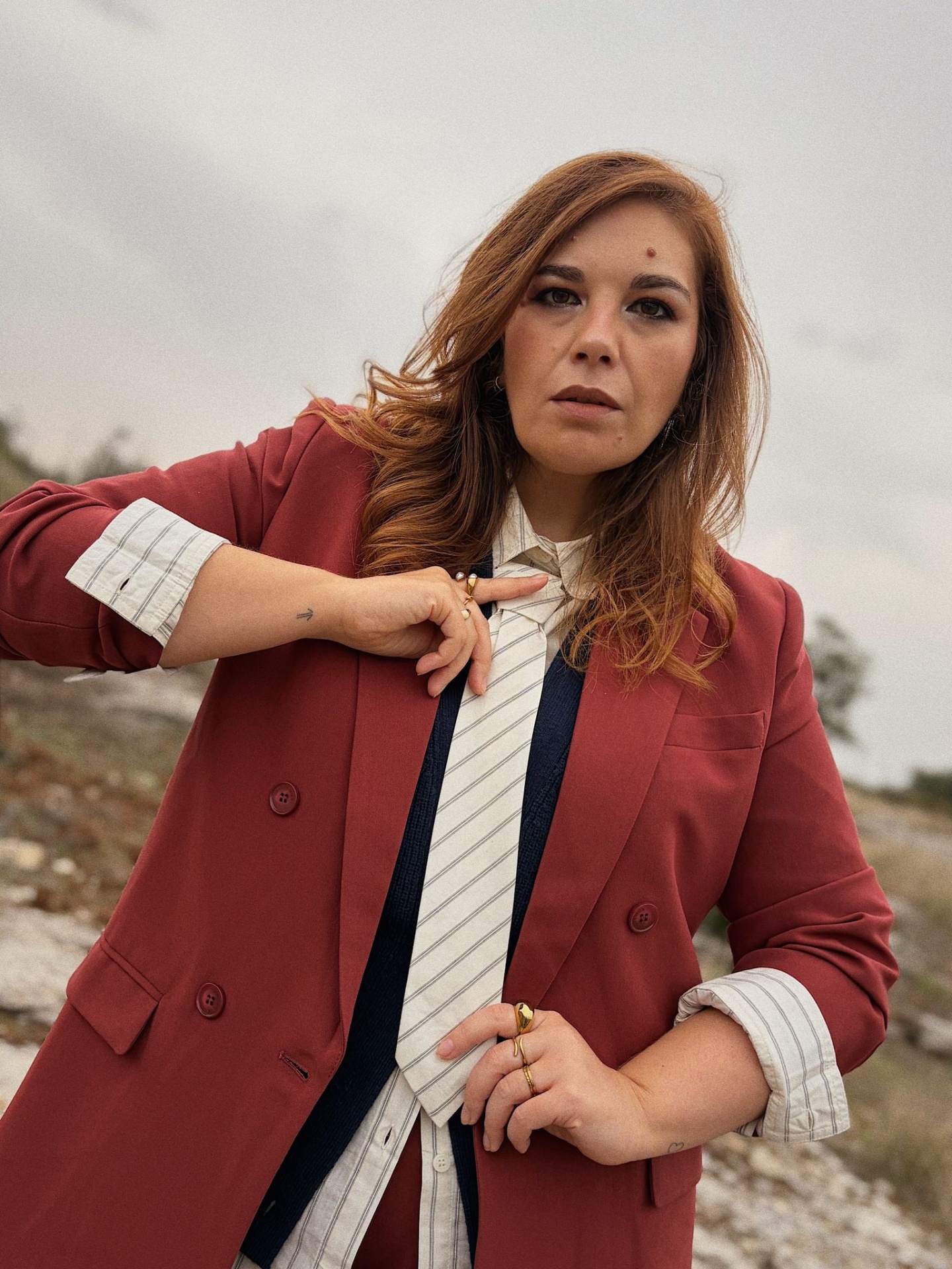CAMISA ATHENA ECRU Mulher com blazer vermelho, camisa branca riscada, colete azul escuro e gravata branca riscada