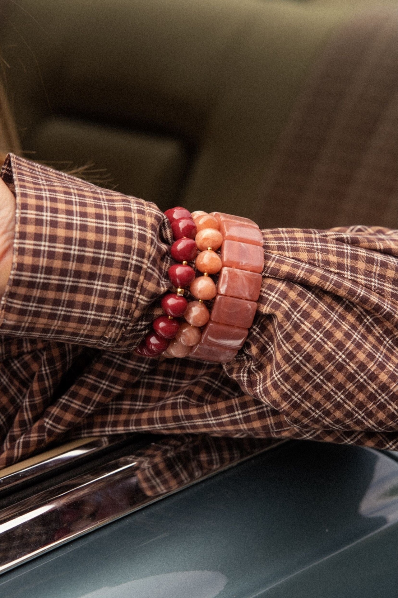 PULSEIRA BRIZIDA Pulseiras de pedras e camisa xadrez castanha junto a superfície metálica