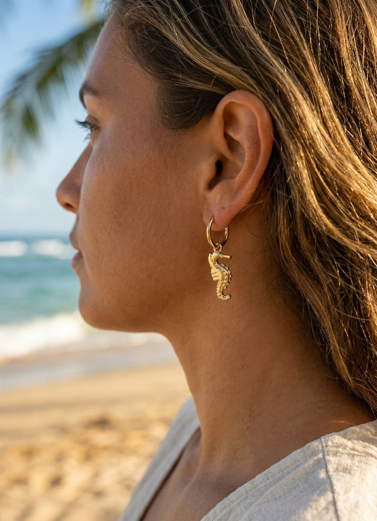 BRINCOS CAVALO Brinco de argola dourada com pendente em forma de cavalo-marinho numa orelha feminina na praia