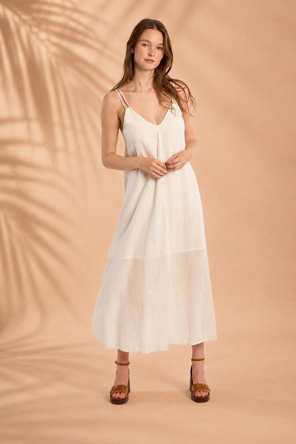 VESTIDO TOMÁSIA Mulher a usar vestido branco de alças finas e sandálias de salto castanhas