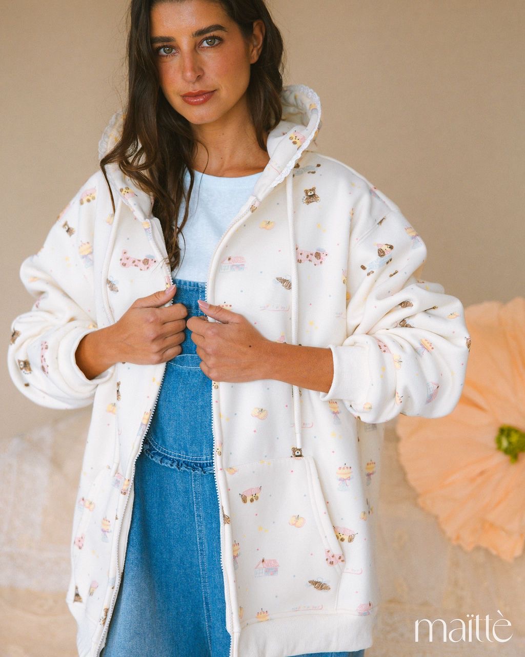 CASACO SIBILA Casaco branco com padrão de desenhos coloridos e capuz, usado por mulher em fundo neutro
