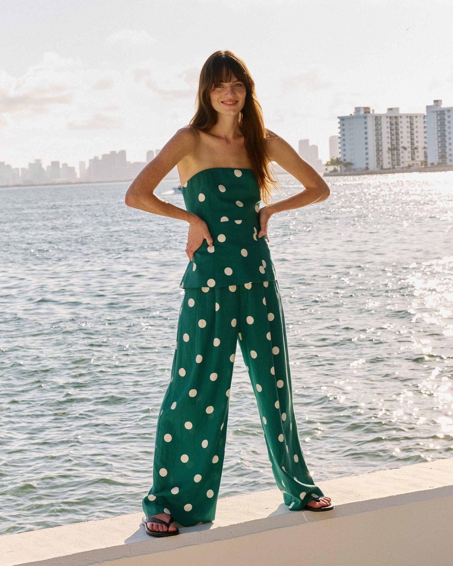 CALÇAS WYNELL VERDE Conjunto verde com bolinhas brancas composto por top e calças largas, usado por mulher junto ao mar.