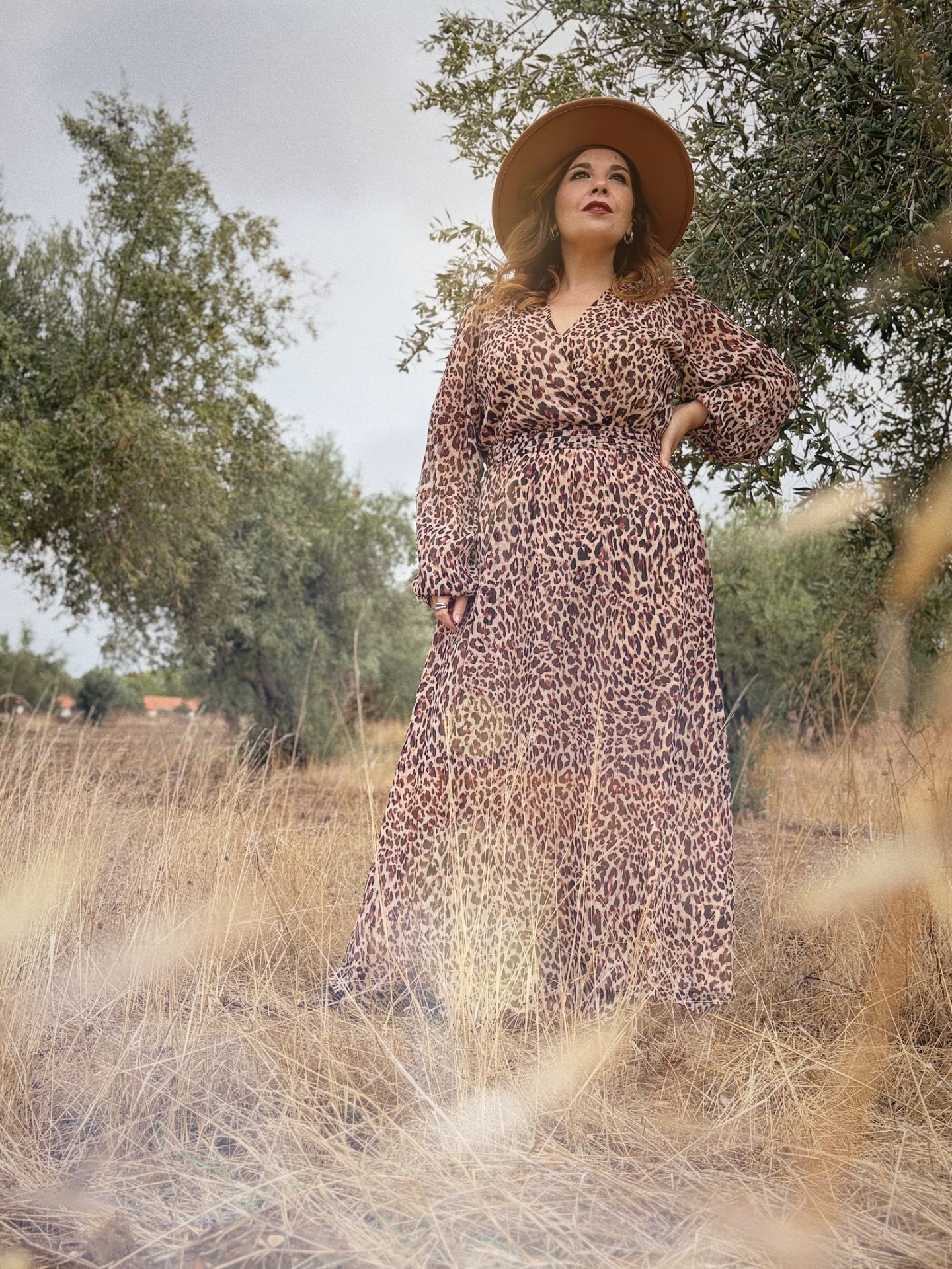 VESTIDO ALICE Mulher com vestido comprido animal print e chapéu castanho em ambiente natural