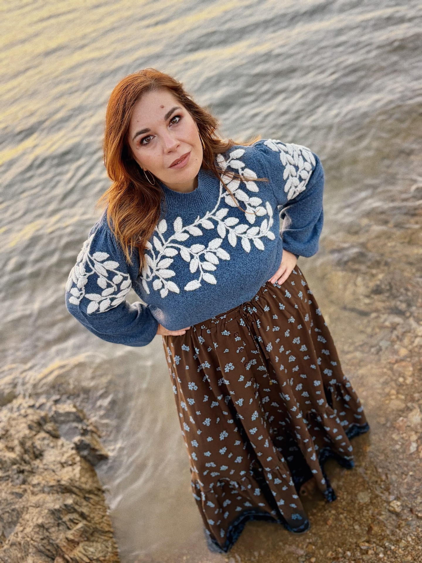 CAMISOLA ARMANDA AZUL Mulher com suéter azul e saia castanha junto a água e rochas