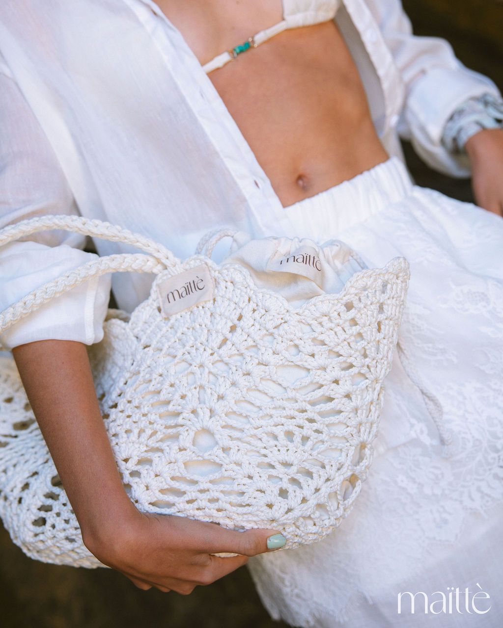 MALA ZILDA Sacola branca de crochê com etiquetas maittè segurada por mulher de roupa branca.