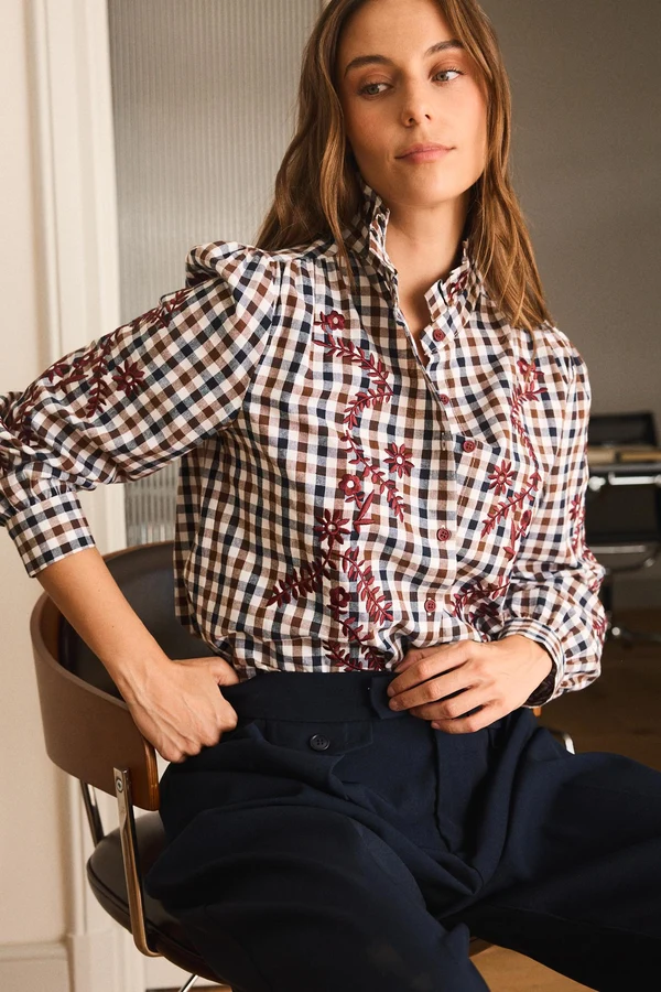 CAMISA MARGAUX Camisa xadrez com bordados florais vermelhos e calças pretas numa cadeira