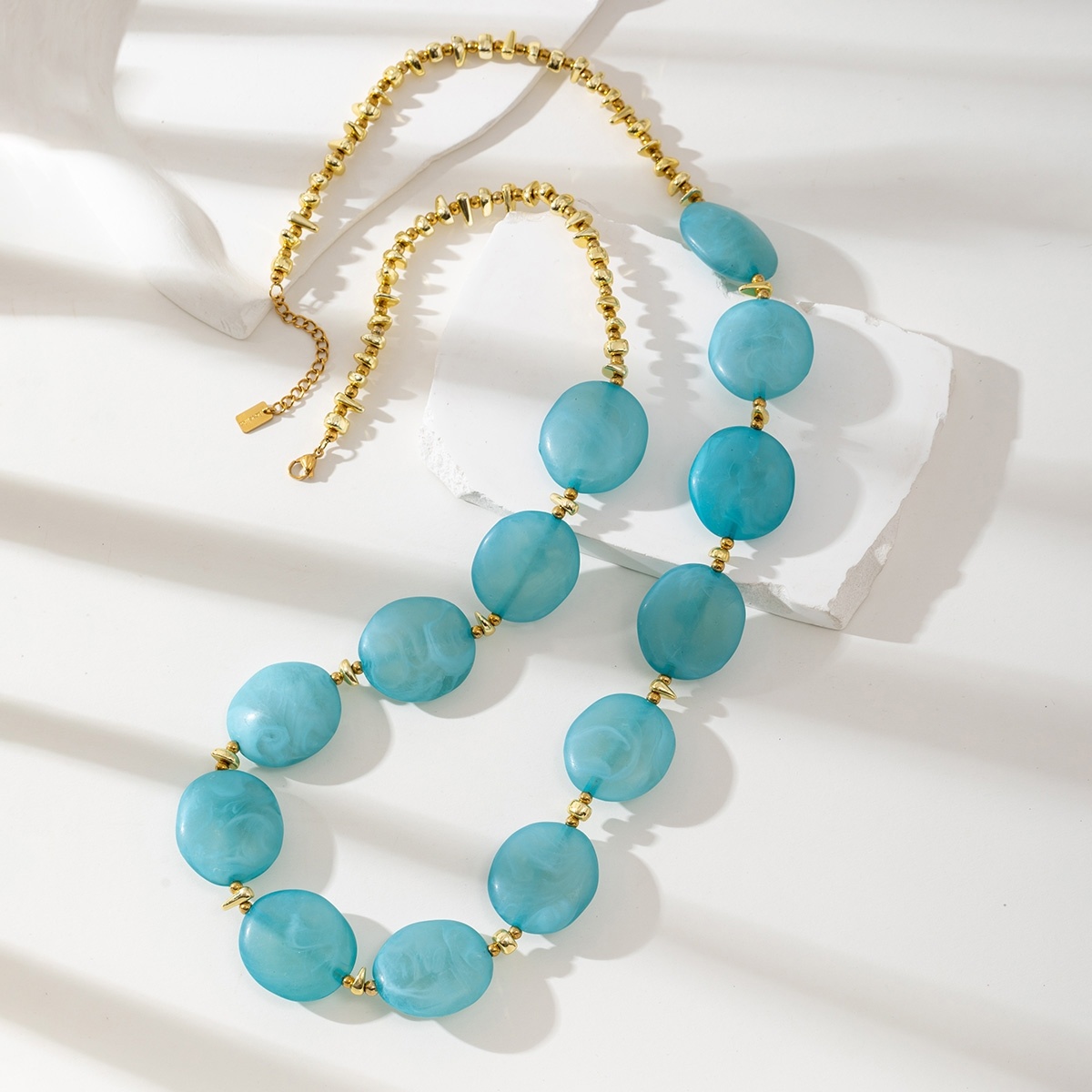 COLAR SELINA Colar com contas azul turquesa e douradas sobre fundo branco