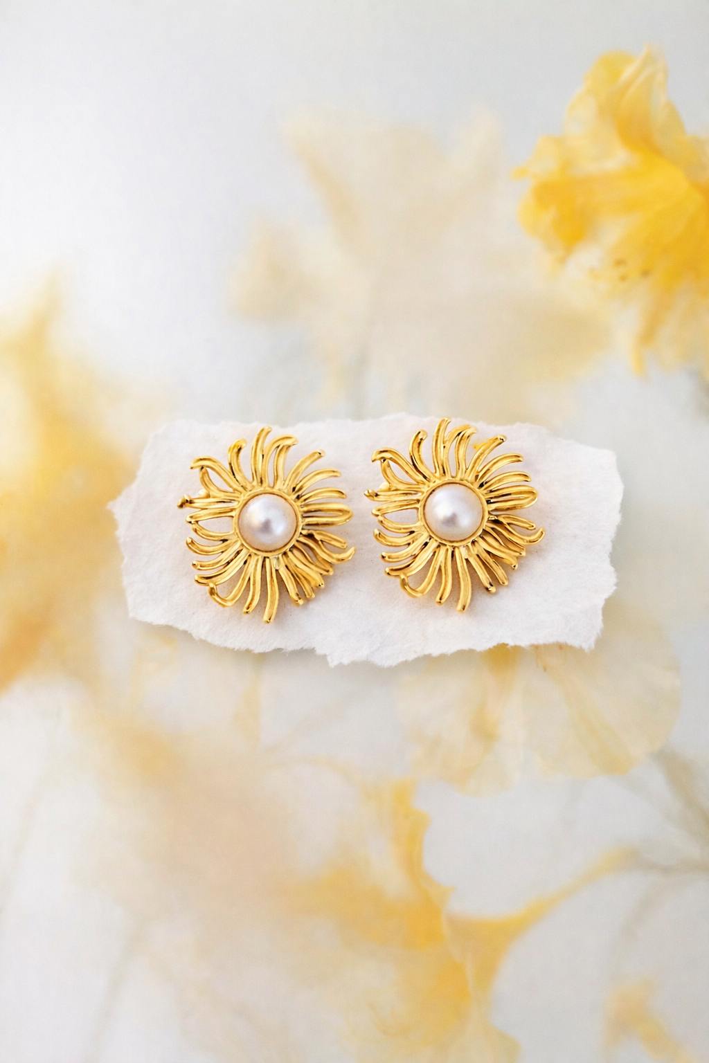 BRINCOS ALFAZEMA Brincos dourados com pérola branca no centro sobre papel branco
