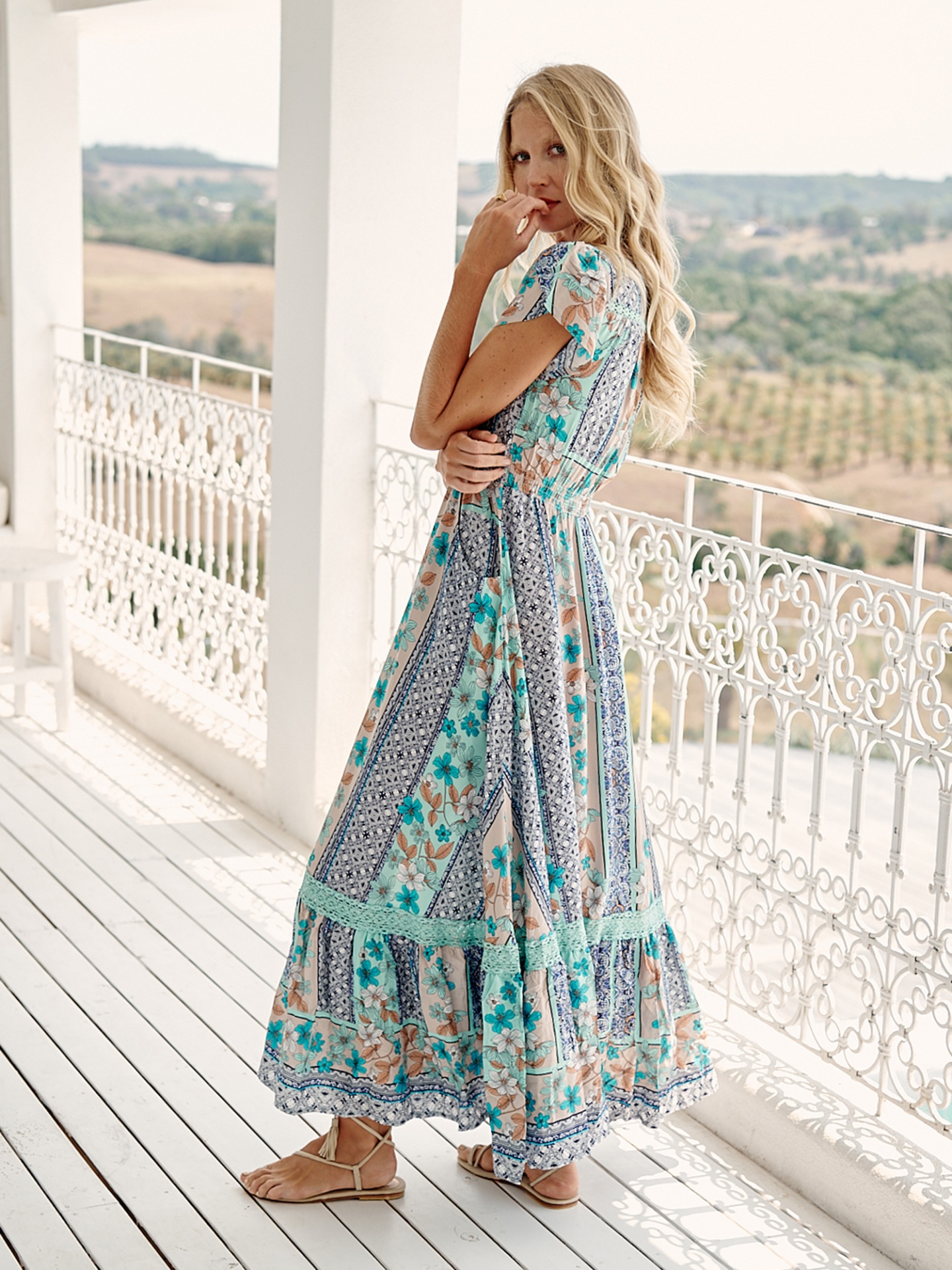 VESTIDO CARLISLE Vestido comprido floral em tons de azul e bege usado por modelo numa varanda branca