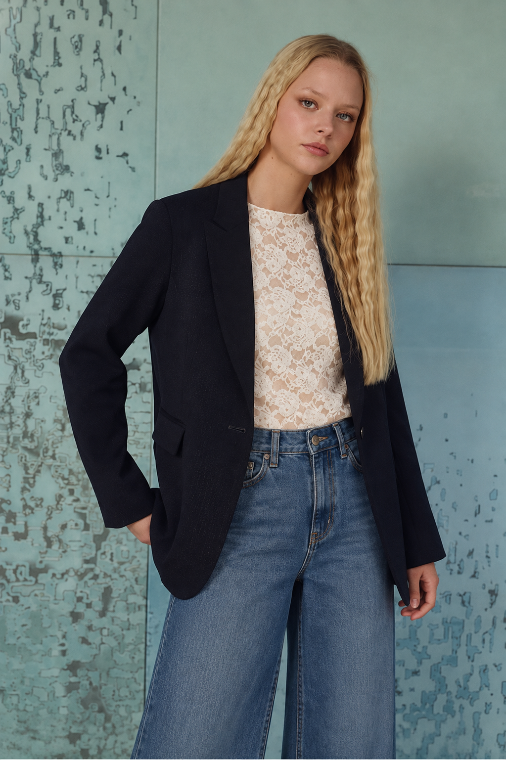 BLAZER BETÂNIA Mulher com blazer preto, blusa rendada branca e jeans azuis de corte largo