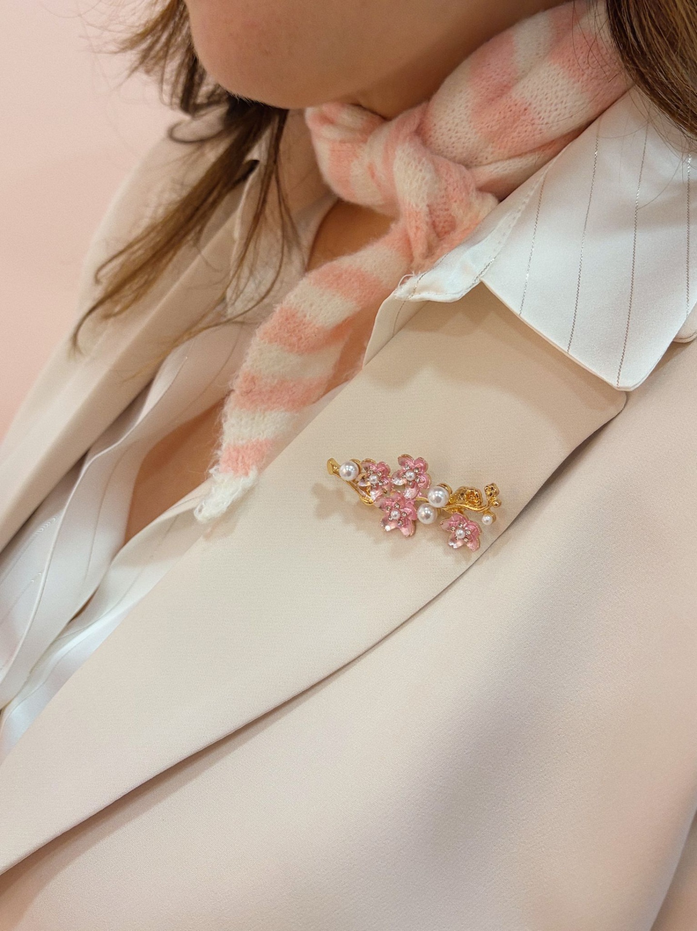 PREGADEIRA PLÍNIA Broche flores rosa e pérolas num blazer bege claro com camisa branca e lenço rosa
