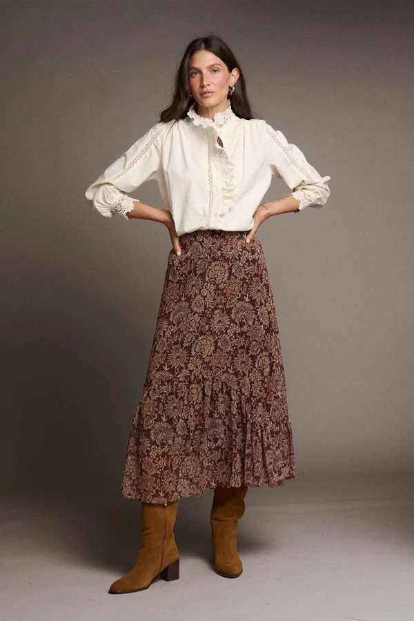 SAIA ELENI Mulher com blusa branca rendada, saia floral castanha e botas castanhas