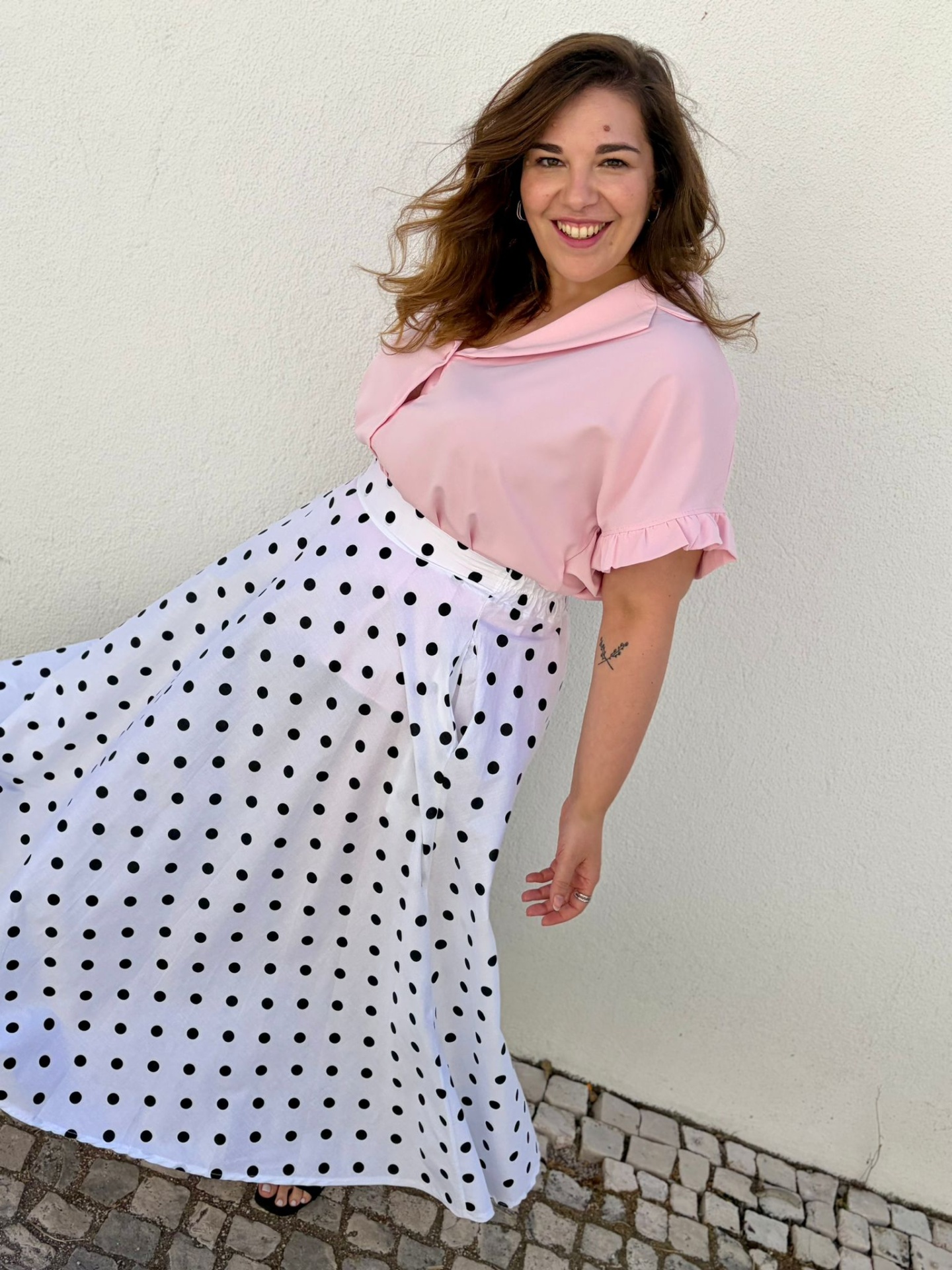 SAIA DOT Vestido rosa claro com saia branca de bolinhas pretas usado por mulher sorridente próximo a parede branca