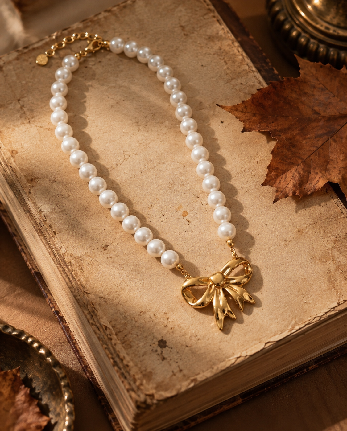 COLAR ANOUK Colar de pérolas com pendente laço dourado sobre livro antigo