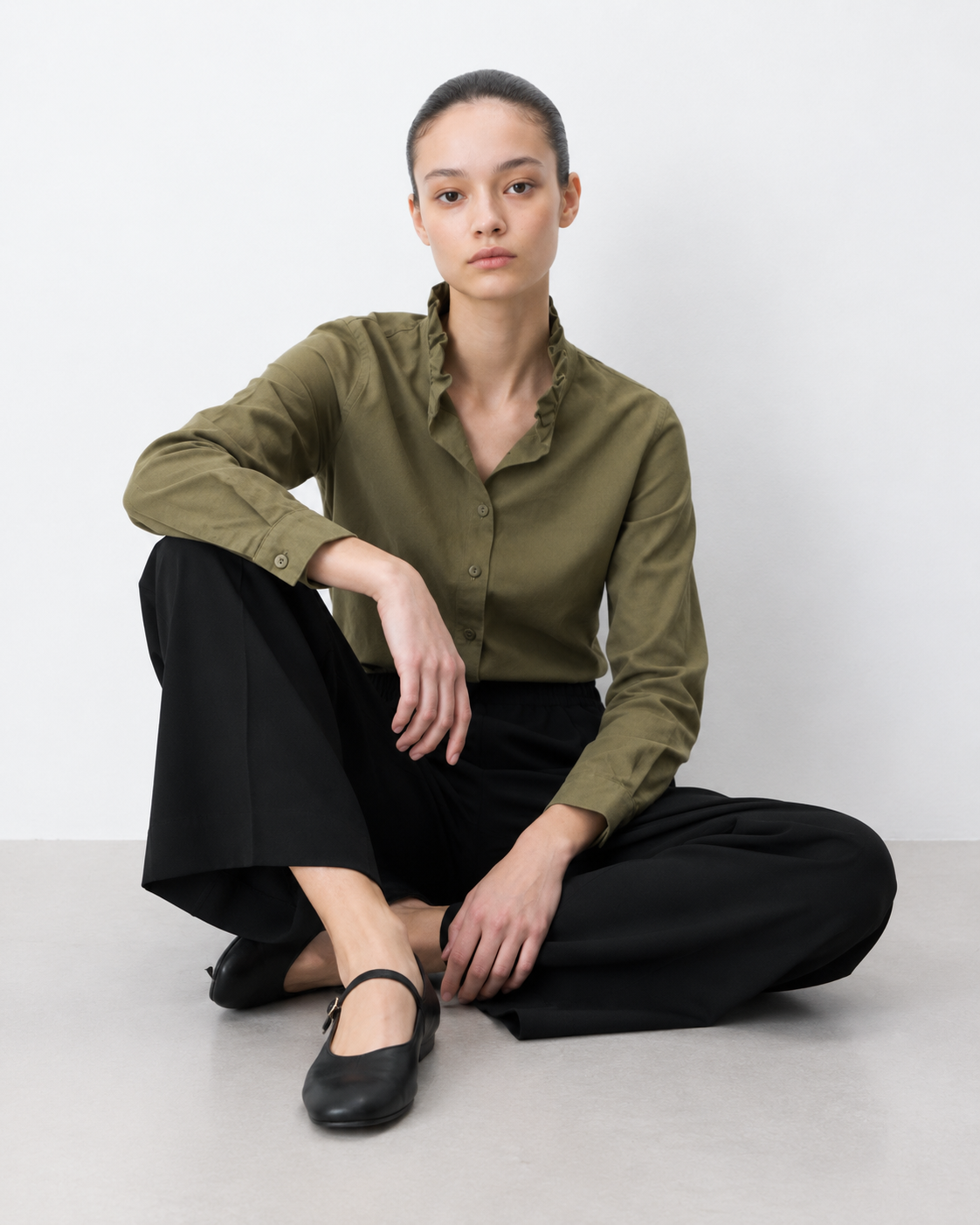 CALÇAS NOBLESSE PRETO Mulher com camisa verde oliva e calças pretas sentada no chão