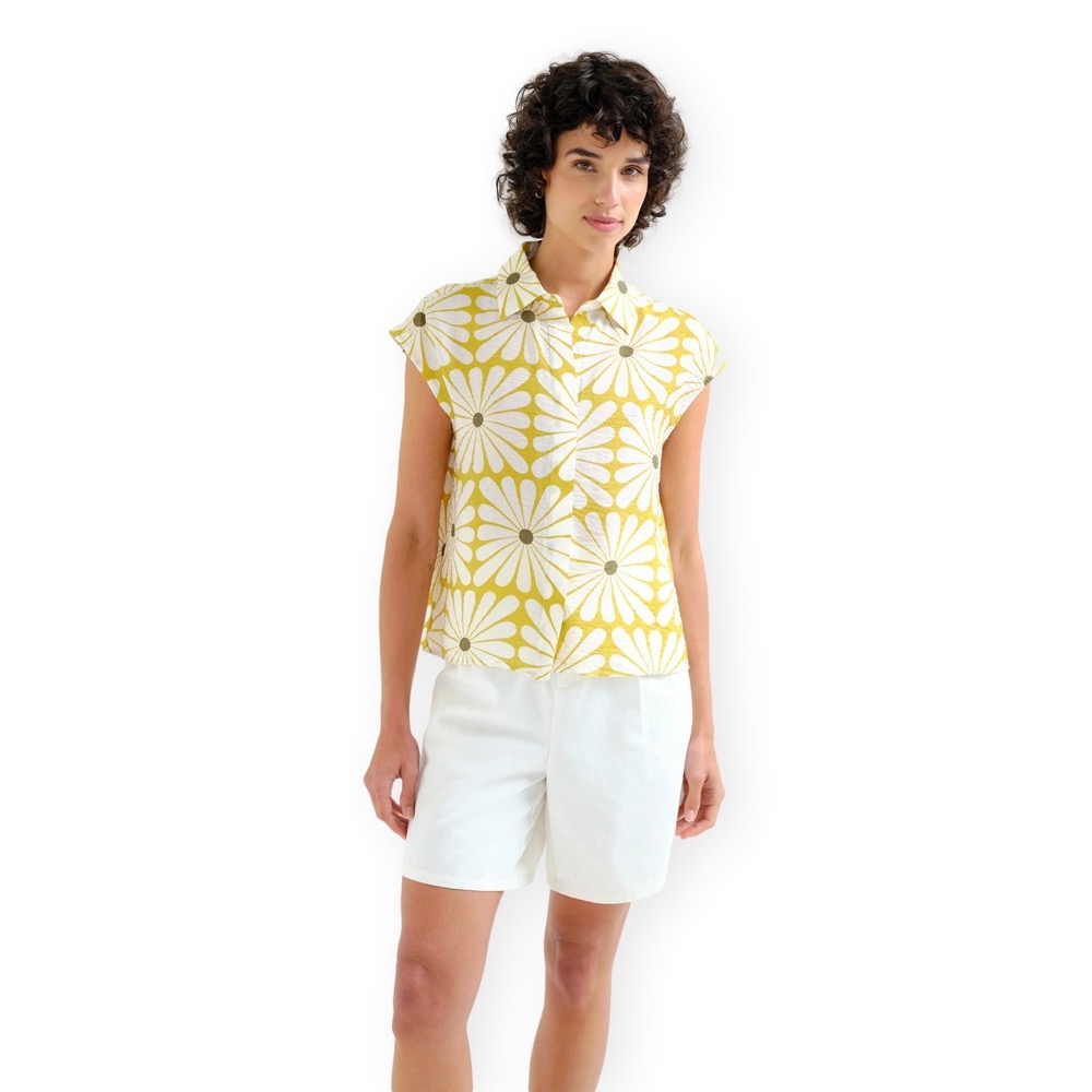 CAMISA WINNIE Mulher com camisa amarela com flores brancas e calções brancos em fundo branco