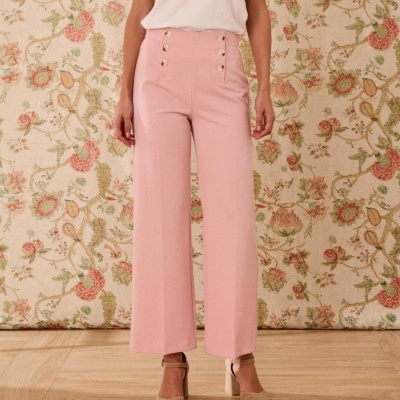 Calças cor-de-rosa com botões, usadas com sapatos bege e t-shirt branca, background floral.