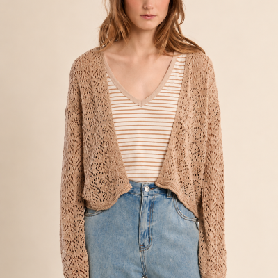 Mulher com cardigan bege de crochê, t-shirt riscada castanha e branca e jeans azuis.