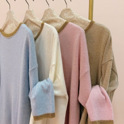 Camisolas de malha coloridas com detalhes dourados penduradas em cabides florais num suporte amarelo