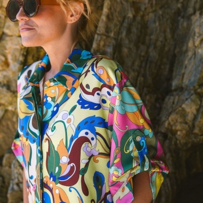 Mulher com óculos de sol e camisa colorida com padrão abstrato perto de rochas.