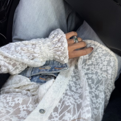 Camisa branca de renda floral e calças de ganga azuis com mão e anel prateado verde