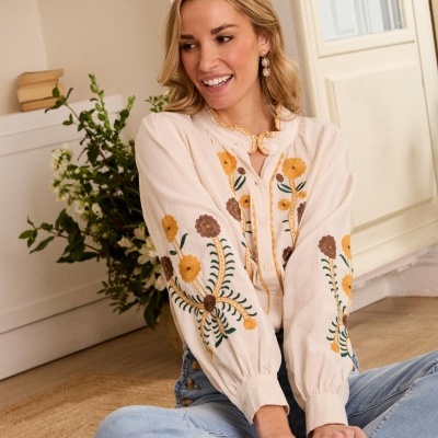 Blusa bege clara com bordados florais coloridos e botões frontais, usada com jeans azul claro